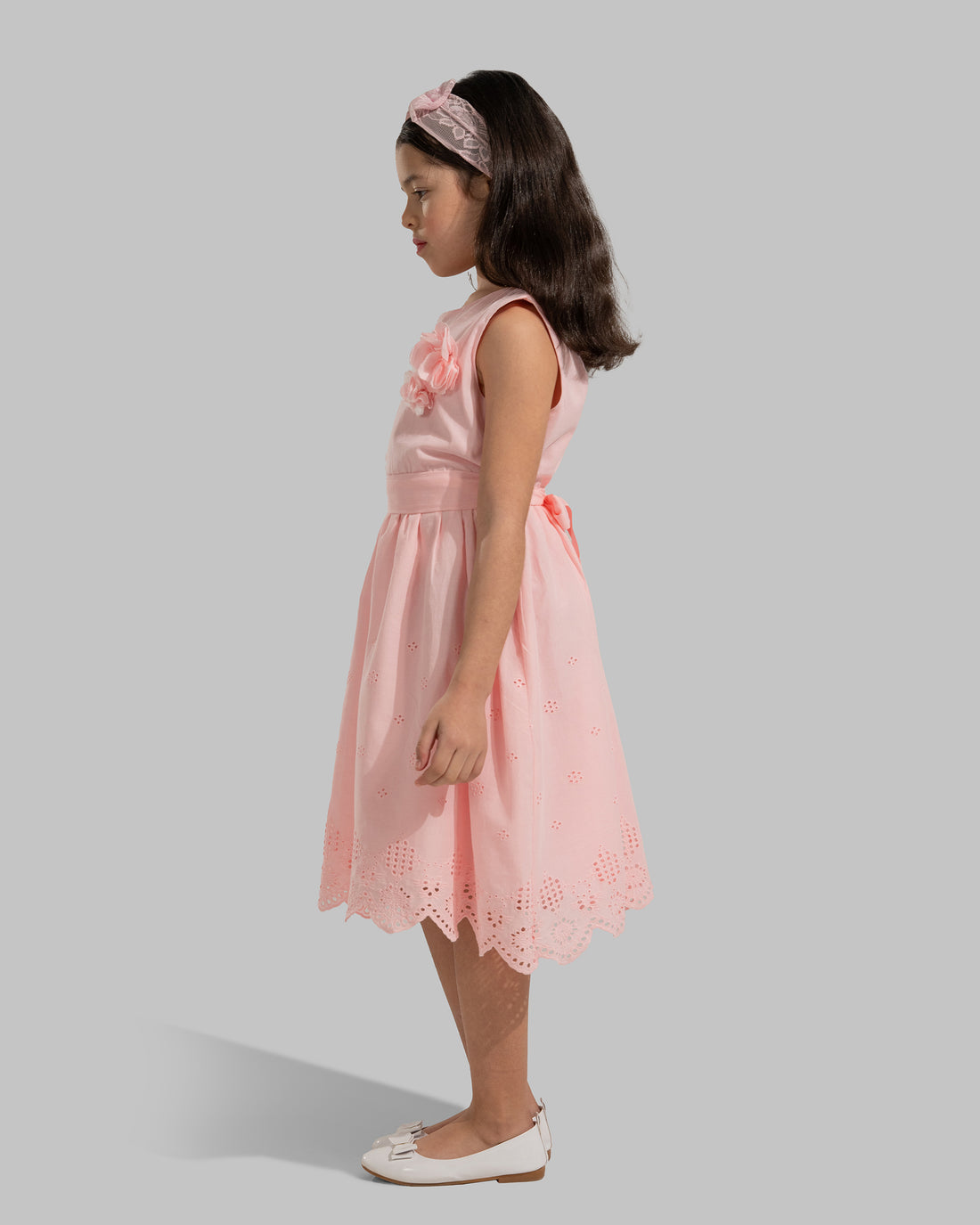 sleeveless pink cotton eyelet dress featuring a floral appliqué on the chest and a matching waist belt.